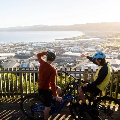 Two cyclists stop at a lookout at Waiu Mountain Bike Park overlooking the city and the harbour below.