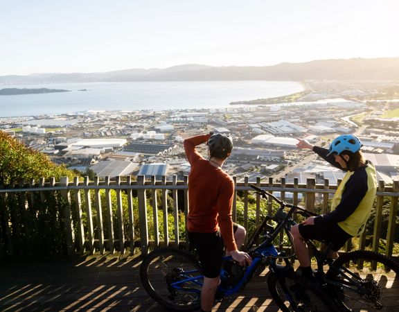 Two cyclists stop at a lookout at Waiu Mountain Bike Park overlooking the city and the harbour below.