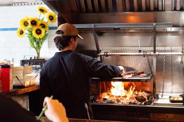 A chef at El Matador grills meats over an open flame.