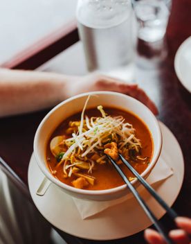 Close up of a person dipping into a bowl of laksa with chopsticks.