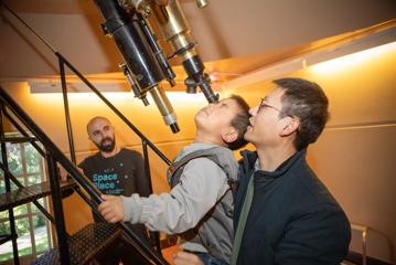 A parent holding up a child to look into the giant telescope at Space Place, Carter Observatory in Wellington.