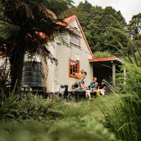 The exterior of Field Hut in Tararua Forest Park. People are sitting on the deck eating. Native trees surround the hut.