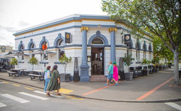 The exterior of Karahui wine bar, light blue and white with gold trim, and customers walking around in front.