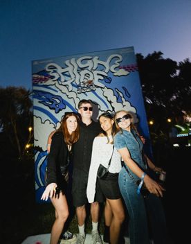Four people pose for a photo-op on a surfboard at High Tide 2024 with the signage behind them.