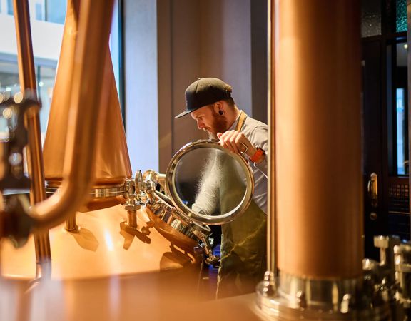 A worker opens a large distilling vat at Woodward Street Distilling Company.