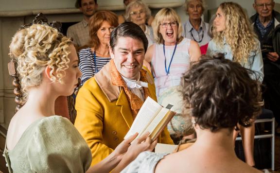 Three members of the New Zealand Opera are rehearsing in costume with a small engaged audience in the background.