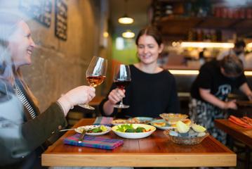 Two customers clink their wine glasses and enjoy their food at Graze Wine bar.