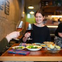 Two customers clink their wine glasses and enjoy their food at Graze Wine bar.