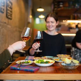 Two customers clink their wine glasses and enjoy their food at Graze Wine bar.