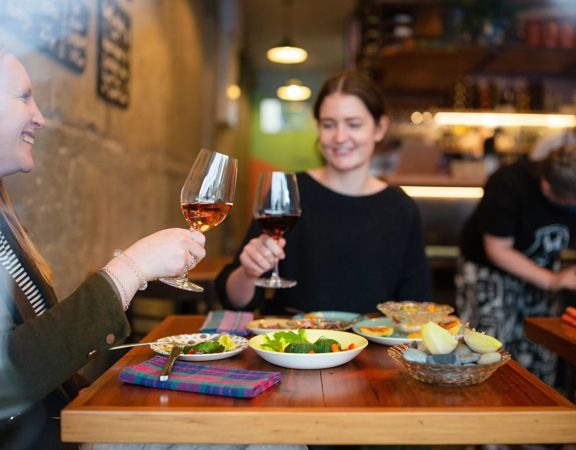 Two customers clink their wine glasses and enjoy their food at Graze Wine bar.