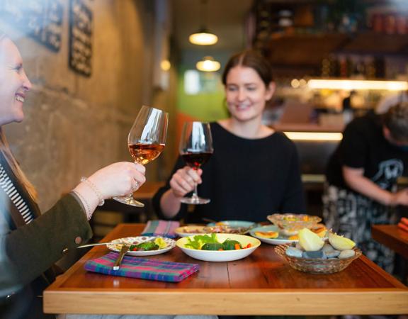 2 customers clink their wine glasses and enjoy their food at Graze Wine bar.
