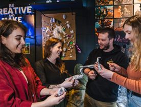 Three people making dinosaurs out of tin foil inside Wētā Workshops, being taught by a smileing team member.