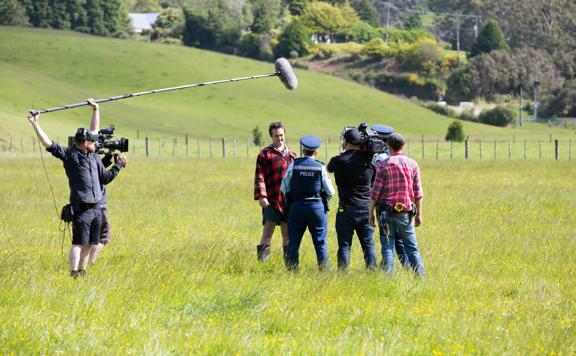 Film crew filming in a green field for Wellington Paranormal. Actors are police man and farmer.