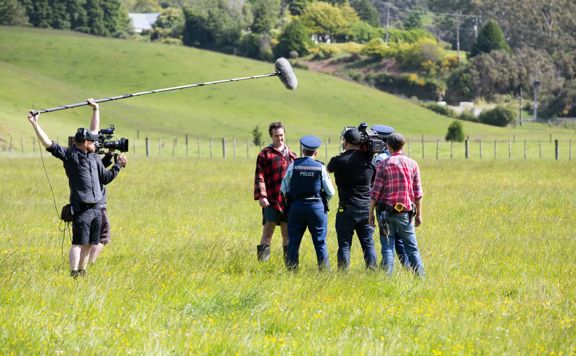 Film crew filming in a green field for Wellington Paranormal. Actors are police man and farmer.