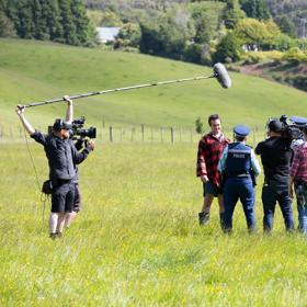 Film crew filming in a green field for Wellington Paranormal. Actors are police man and farmer.