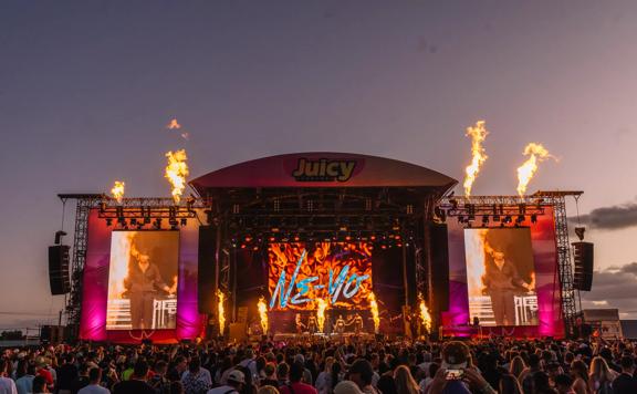 The artist Ne-yo is performing on a big stage with pyrotechnics at Juicy Fest to a full audience.