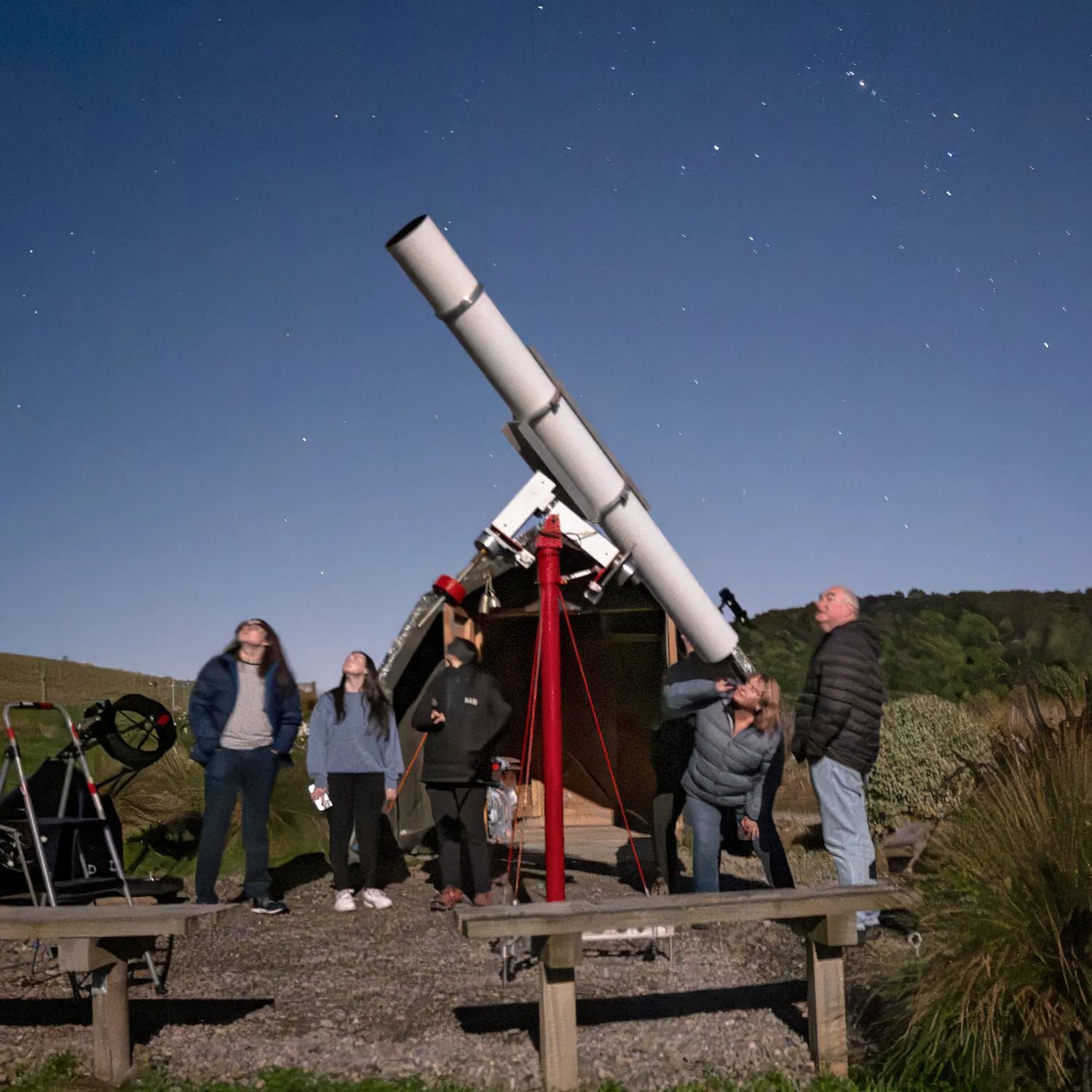 Star Safari visitors look up at the clear night sky using a large telescope.