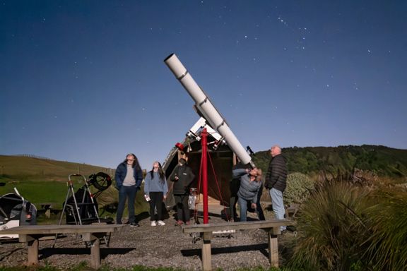 Star Safari visitors look up at the clear night sky using a large telescope.