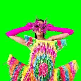 A model poses wearing a colourful fringe dress and hot pink sunglasses on a bright green background.