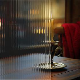 A lit candlestick behind fluted glass.