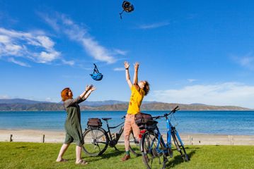 Two people throwing their helmets into the sky standing next to bikes at Scorching Bay Beach.