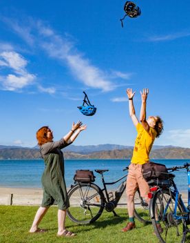 Two people throwing their helmets into the sky standing next to bikes at Scorching Bay Beach.