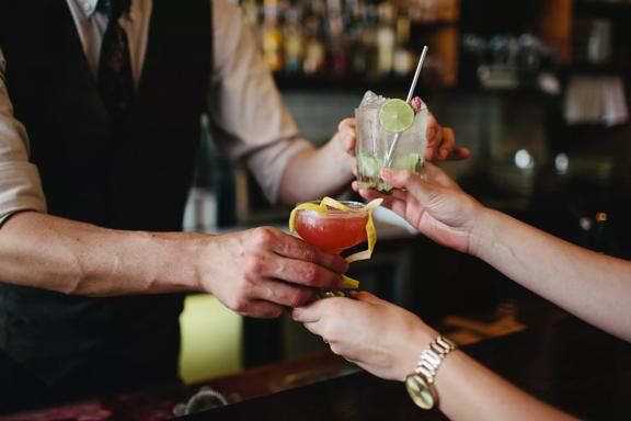 A bartender is handing two cocktails to a patron at Crumpet, a cocktail and wine bar located at the Opera House in Te Aro, Wellington.