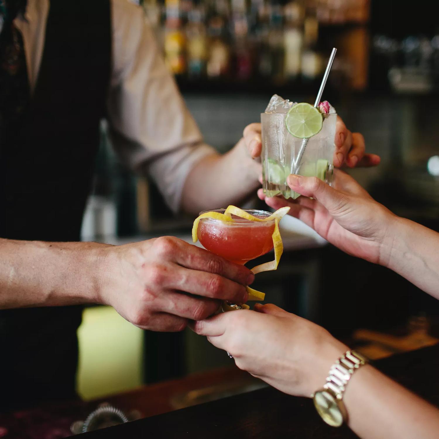 A bartender is handing two cocktails to a patron at Crumpet, a cocktail and wine bar located at the Opera House in Te Aro, Wellington. 