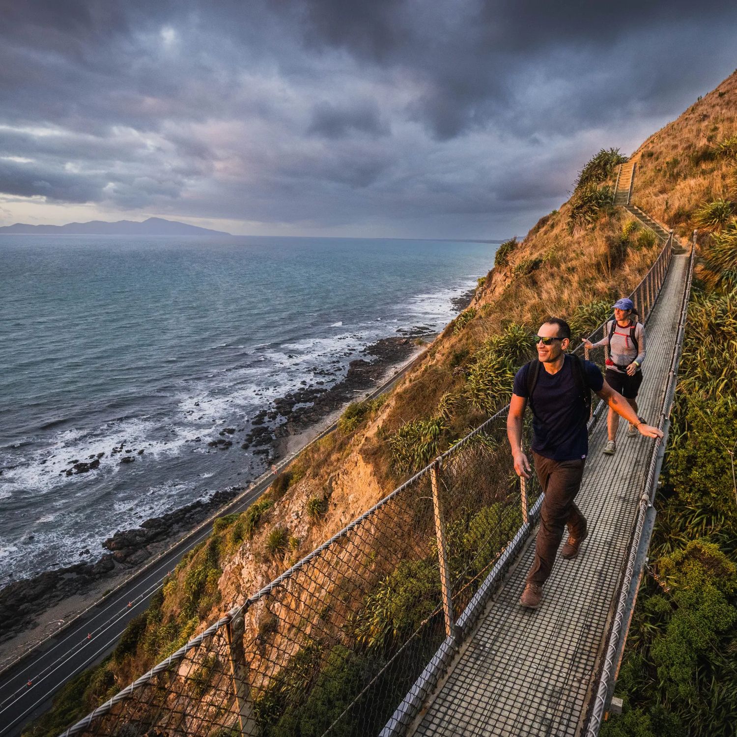Two people walking along a swing bridge between two hillsides on the Escarpment track above the Kāpiti Coast.
