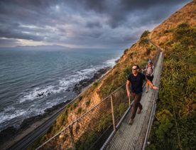 Two people walking along a swing bridge between two hillsides on the Escarpment track above the Kāpiti Coast.