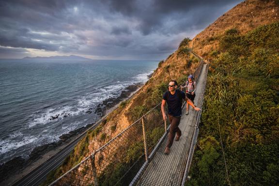 Two people walking along a swing bridge between two hillsides on the Escarpment track above the Kāpiti Coast.