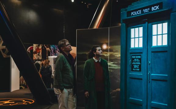 Two people looking up at the Tardis. The Tardis is navy blue and resembles a police public call box.