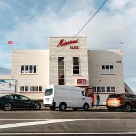 The exterior of Maranui Café, inside the Lyall Bay surf lifesaving club. The building is white with red accents and cars are parked outside.