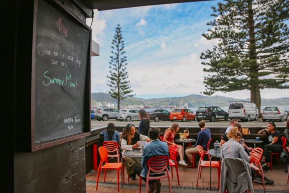 The patio at Beach Babylon Cafe in Oriental Bay, Wellington. There are five small circular tables with two people sitting at each of them.