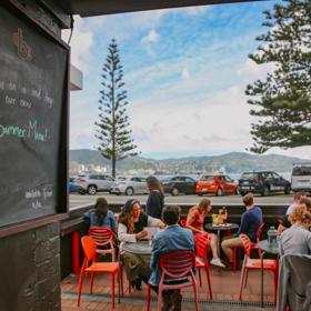 The patio at Beach Babylon Cafe in Oriental Bay, Wellington. There are five small circular tables with two people sitting at each of them.