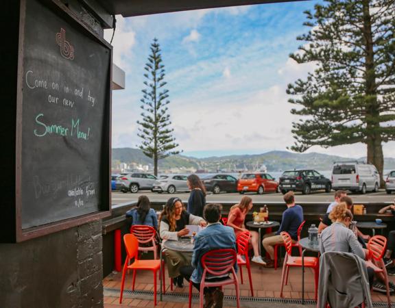 The patio at Beach Babylon Cafe in Oriental Bay, Wellington. There are five small circular tables with two people sitting at each of them.