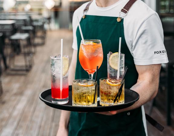 Waiter holding a tray with five colourful cocktails on it.
