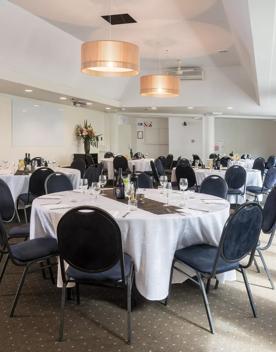 A meeting room inside West Plaza Hotel, with tables and chairs set up for a dining feel and large whiteboards on the walls.