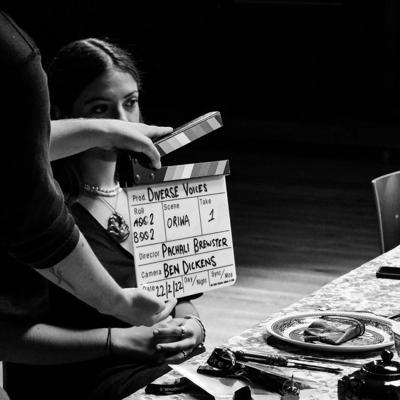 Person sitting on set of Diverse Voices with a clapper board in front of their face.