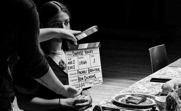 Person sitting on set of Diverse Voices with a clapper board in front of their face.
