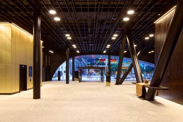 The entrance foyer at Tākina Wellington Convention and Exhibition Centre. The space has high ceilings with exposed beams, beige tile floor and other modern architectural features.