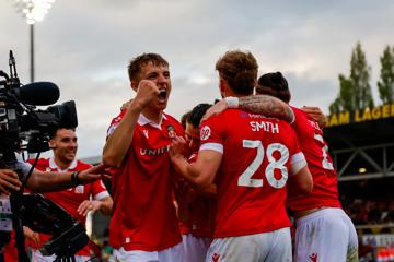 Players of Wrexham AFC huddle in celebration. They wear red shirts and white shorts.