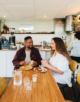 Two people sharing coffee and a meal inside Swimsuit on Dixon Street. The coffee counter is behind them with baristas working.