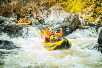 Two rafts carrying two people each hit some rapids in a river.