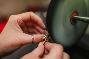 A close-up of a person’s hands holding a diamond ring up to a jewellery polisher.