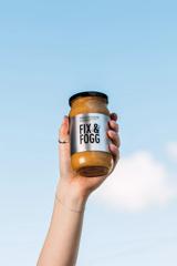 A hand holding a jar of Fix & Fogg peanut butter in the air.