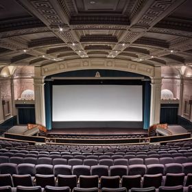 Inside a cinema inside Embassy Theatre. The large auditorium has high vaulted ceilings,  art deco reliefs on the walls and a large projection screen with open teal curtains.