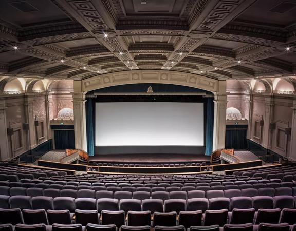 Inside a cinema inside Embassy Theatre. The large auditorium has high vaulted ceilings,  art deco reliefs on the walls and a large projection screen with open teal curtains. 