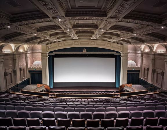 Inside a cinema inside Embassy Theatre. The large auditorium has high vaulted ceilings,  art deco reliefs on the walls and a large projection screen with open teal curtains.