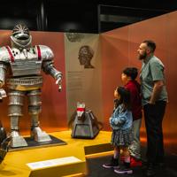 An adult and two children look at three robots on display at the Doctor Who Worlds of Wonder exhibition. 